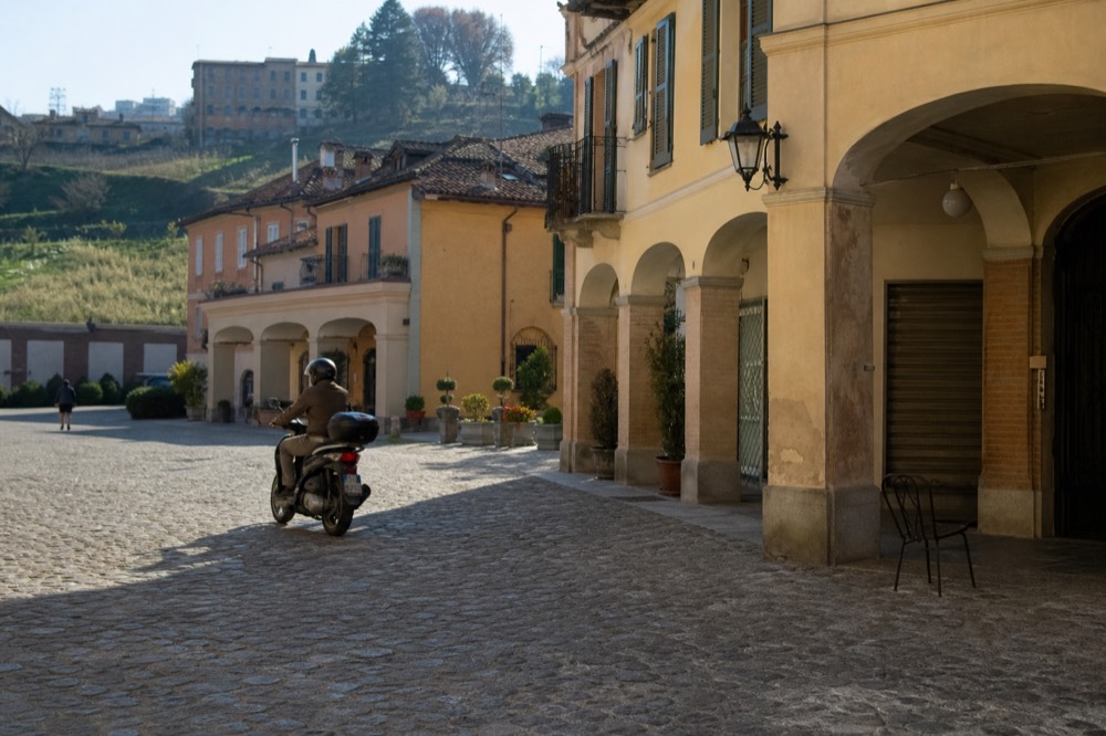 E-bike rider wearing a helmet rolling through a sunlit village piazza.