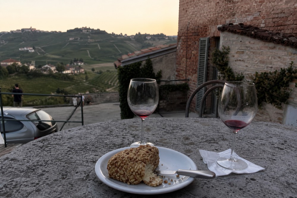 Wine glasses and a plate of local cheese on a terrace overlooking vineyards.