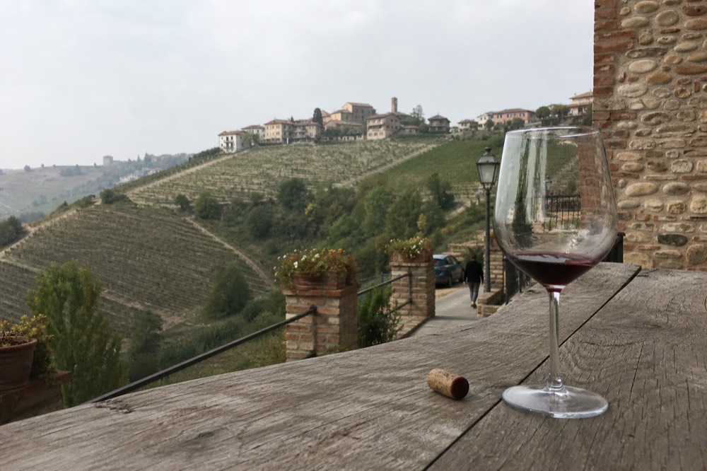 A glass of red wine on a wooden table overlooking terraced vineyards.