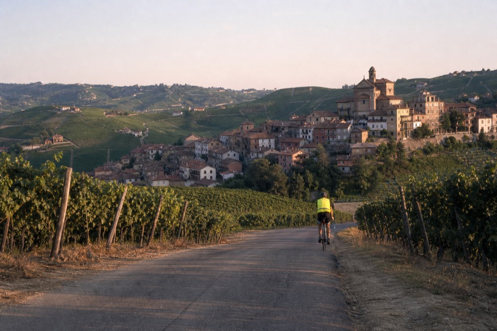 A cyclist on an e-bike riding a quiet road between vineyard rows.