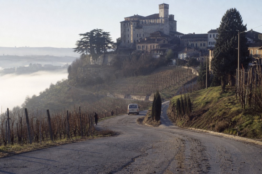 Vineyard roads climbing from the valley toward a Langhe hilltop village.
