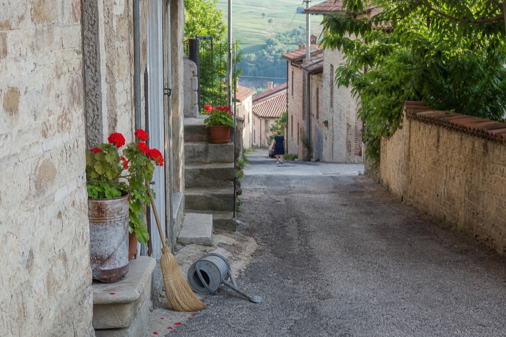 A quiet Langhe village street with stone buildings and flowers.