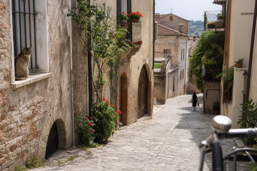Cobblestone village street in a Langhe hilltown with stone houses and flowers.