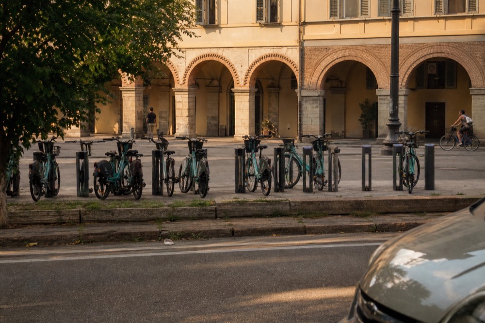 A row of rental bicycles parked on a Turin street near an arcade.