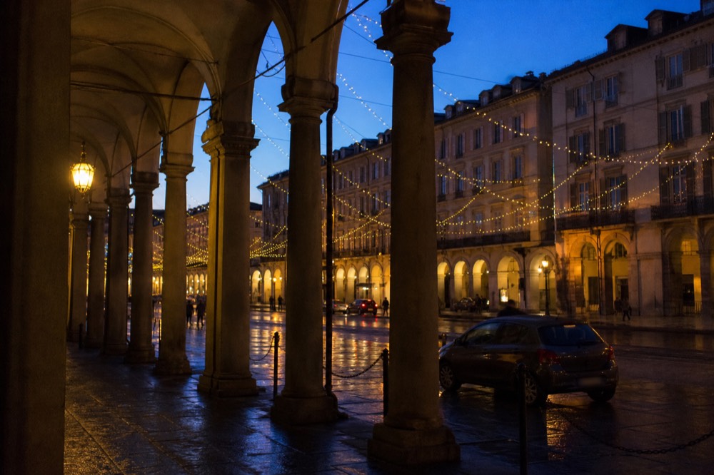 Lit arcades and street installations of a winter light festival in Turin at dusk.