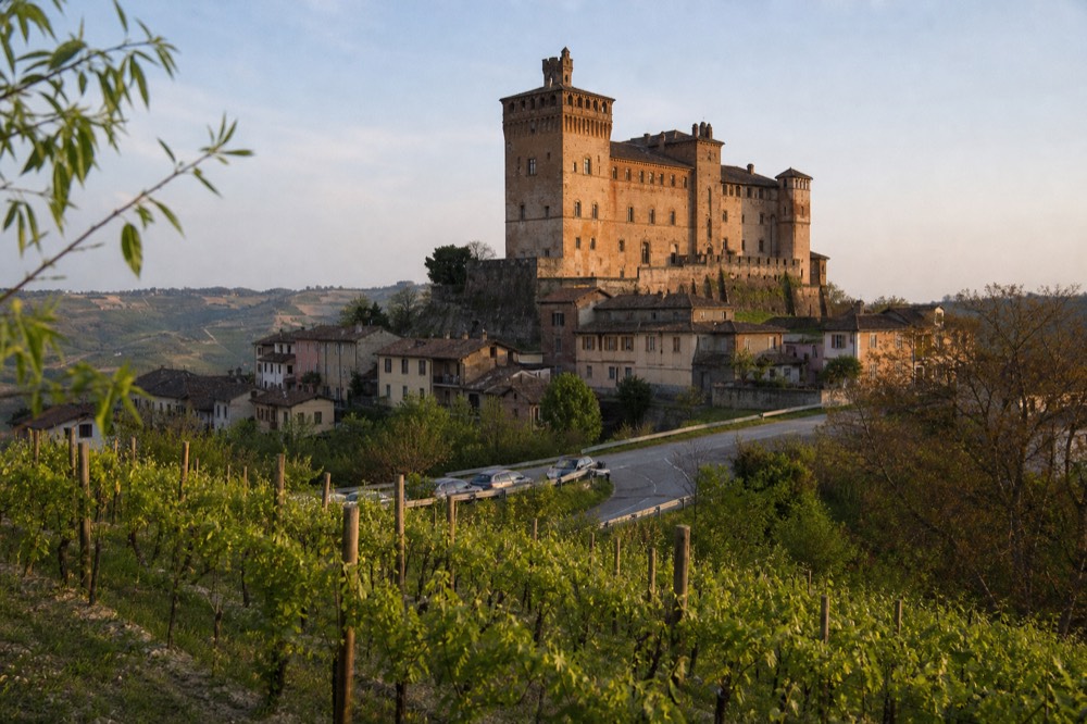 A slender turreted castle above a small stone village and vineyard slopes.