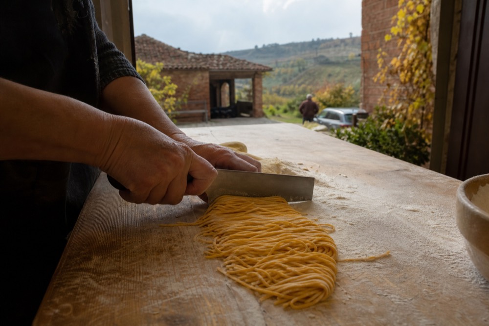 Golden tajarin pasta being cut by hand on a floured wooden board.