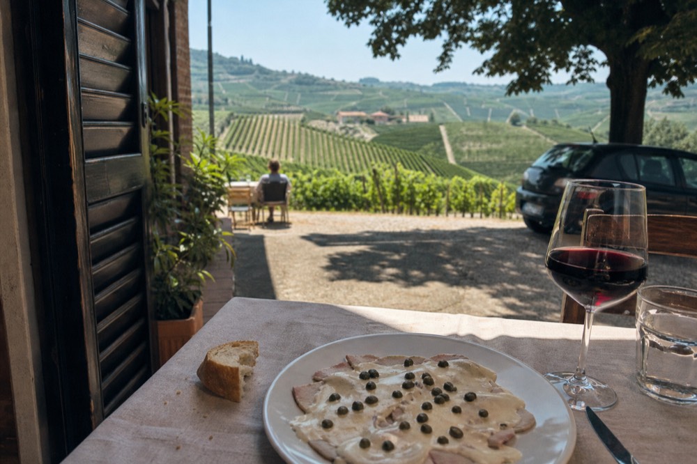 A rustic table set with vitello tonnato and a glass of red wine in a Langhe trattoria.