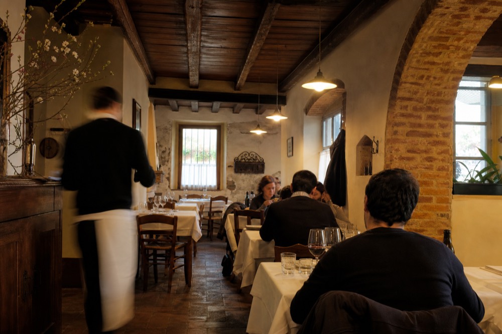 A traditional Piemontese trattoria interior with wooden tables set for dinner.