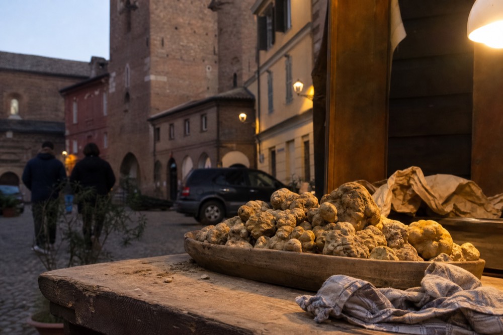 A rustic market stall with fresh white truffles in a wooden bowl.