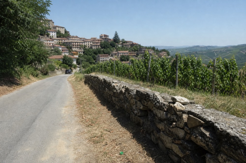 E-bike leaning against a stone wall beside a vineyard road with hills beyond.