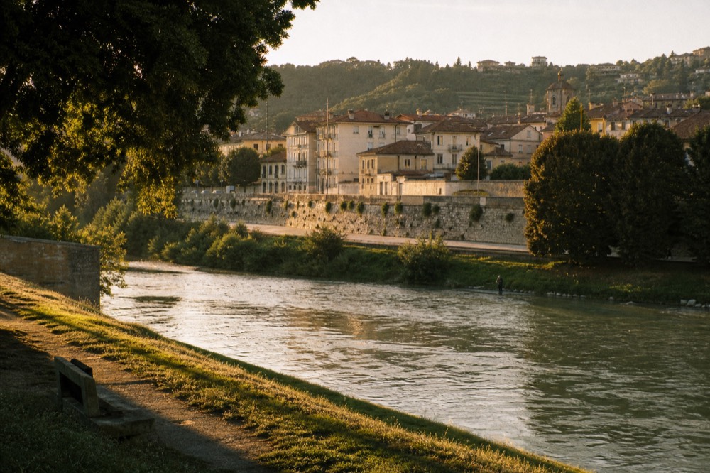 Tanaro river flowing past Alba's riverside with wooded hills behind.