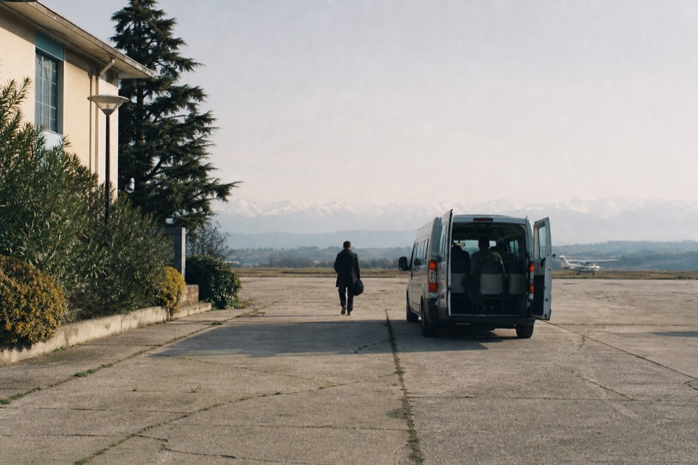 Small regional airport terminal building on a plain with the Alps on the horizon.