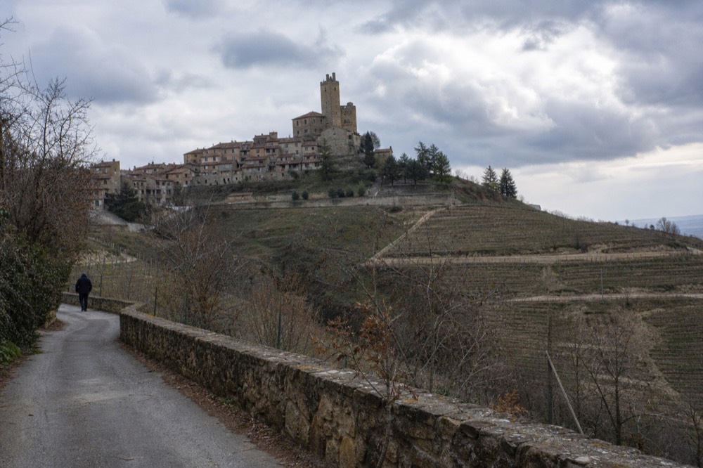 Narrow rural lane curving between terraced vineyards with a small stone village on the ridge.