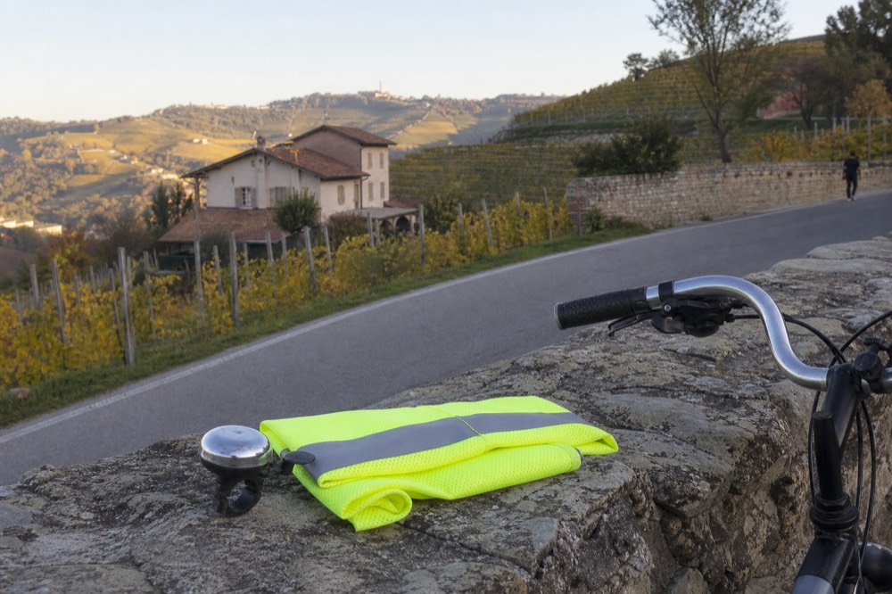 A bicycle bell and reflective vest resting on a stone wall beside a country road.