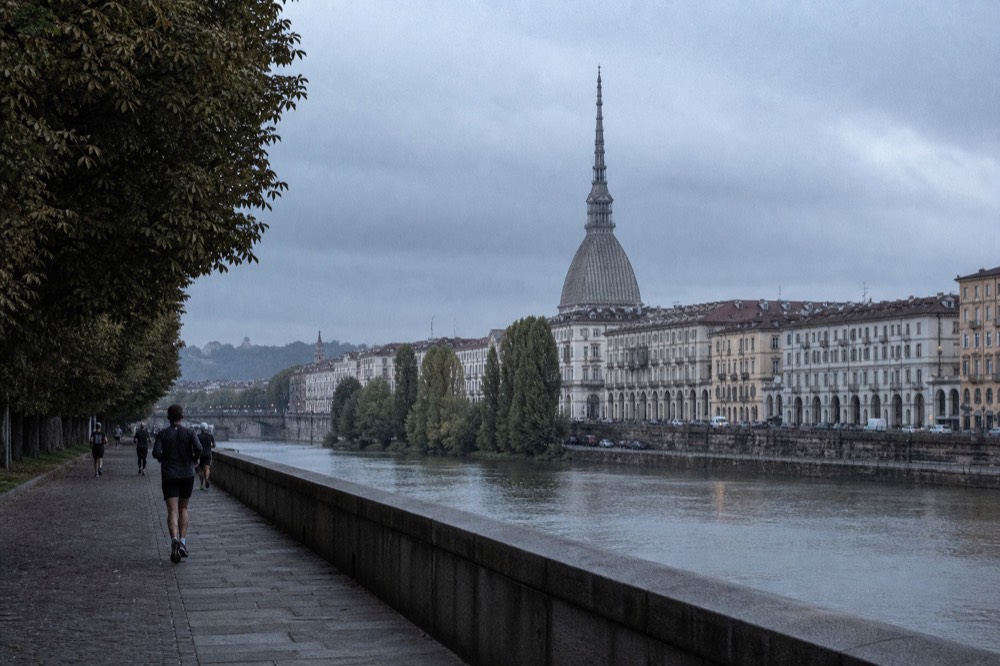 Turin's Mole Antonelliana and arcaded streets seen from a riverside path.