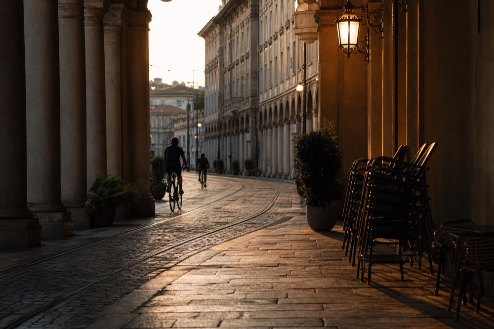 Cyclists on a Turin arcade-lined street in evening light.