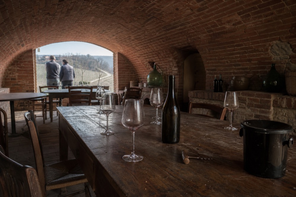A tasting table set with wine glasses and a corkscrew in a small cellar.