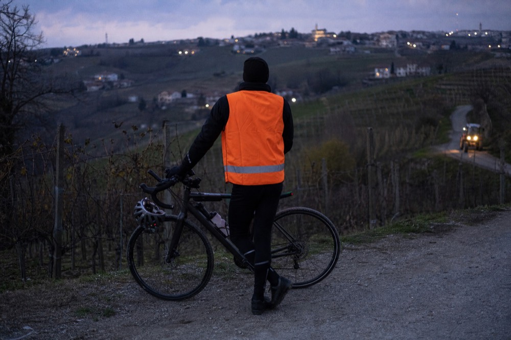 A cyclist with a reflective vest resting beside vineyards at dusk.